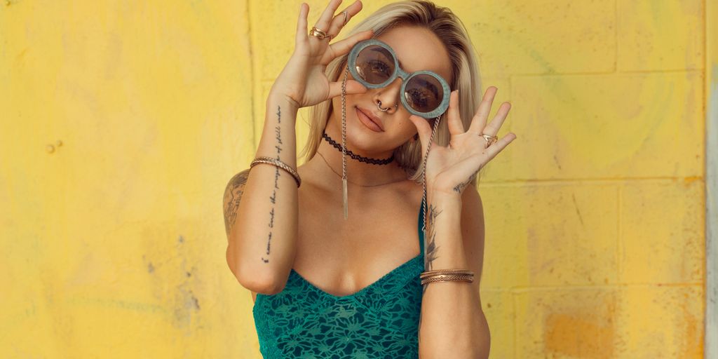 woman in blue bralette holding sunglasses putting on her eyes